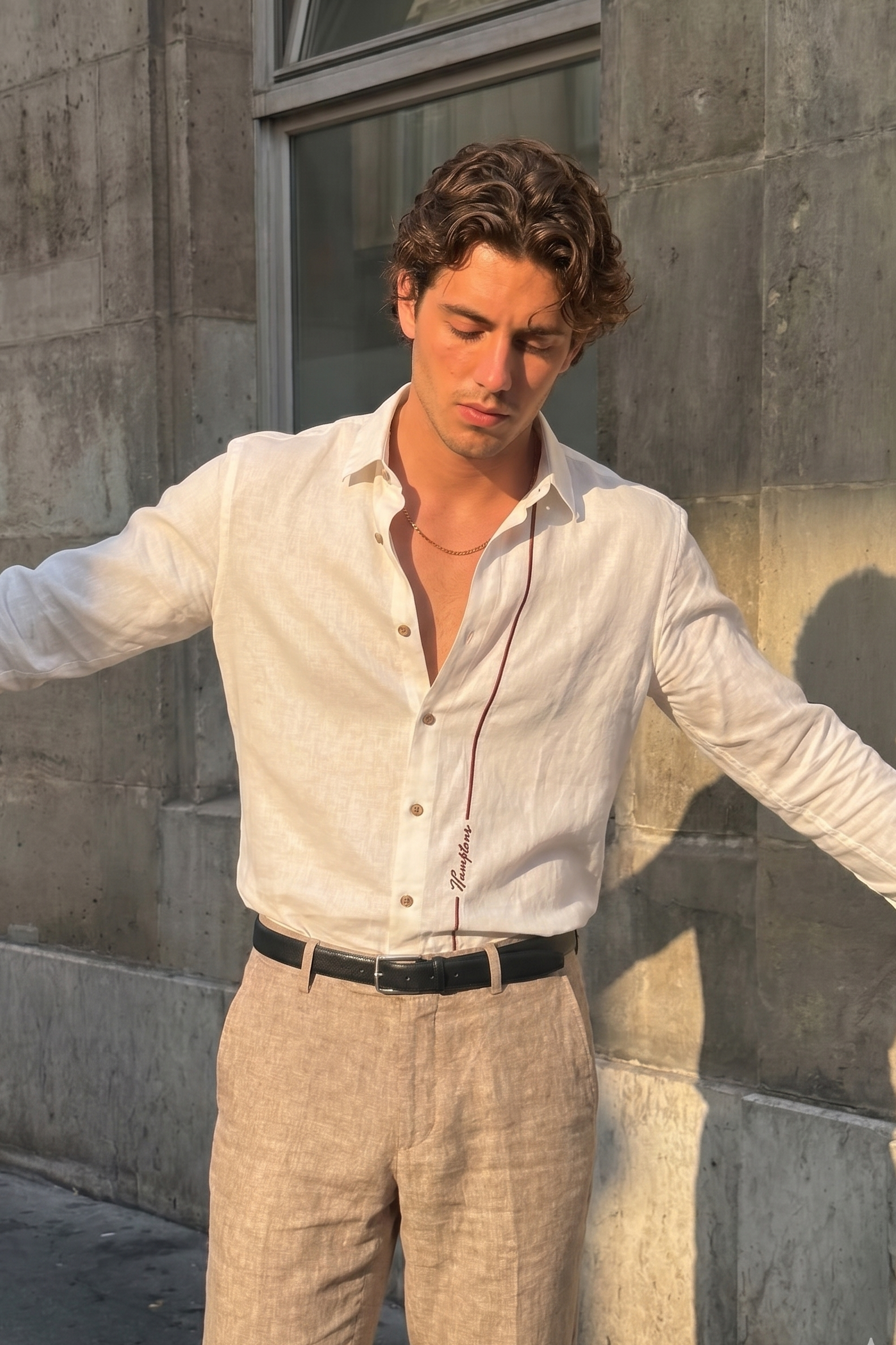 Man wearing a white shirt and beige pants standing against a stone wall.